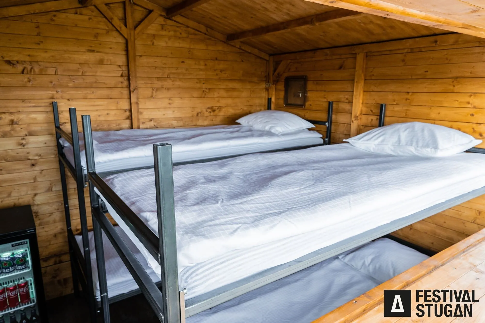 Stuga med våningssäng med vita lakan och en minikyl