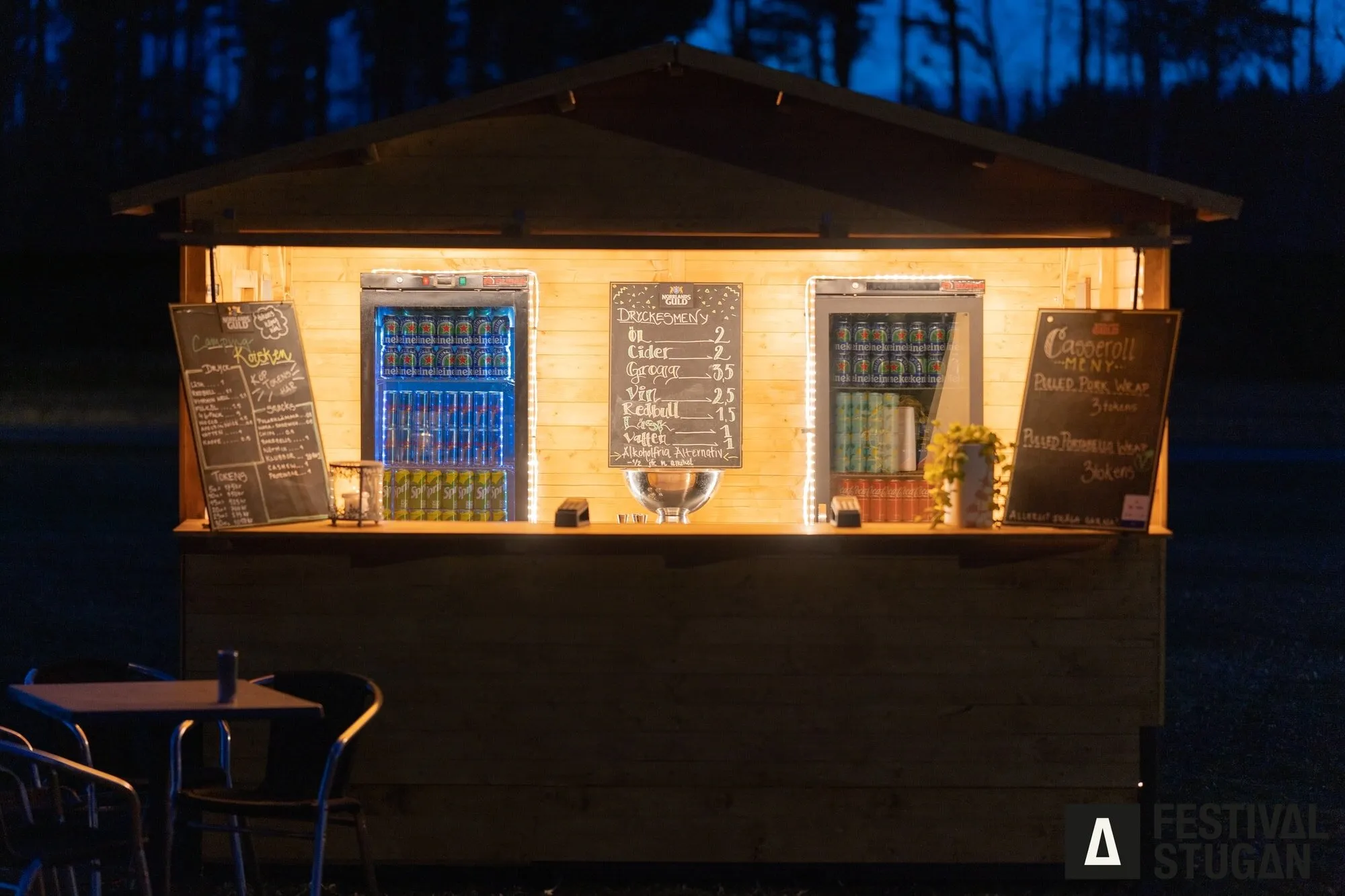 Stugan som bar i skymningen, med menytavlor och dryckeskylar