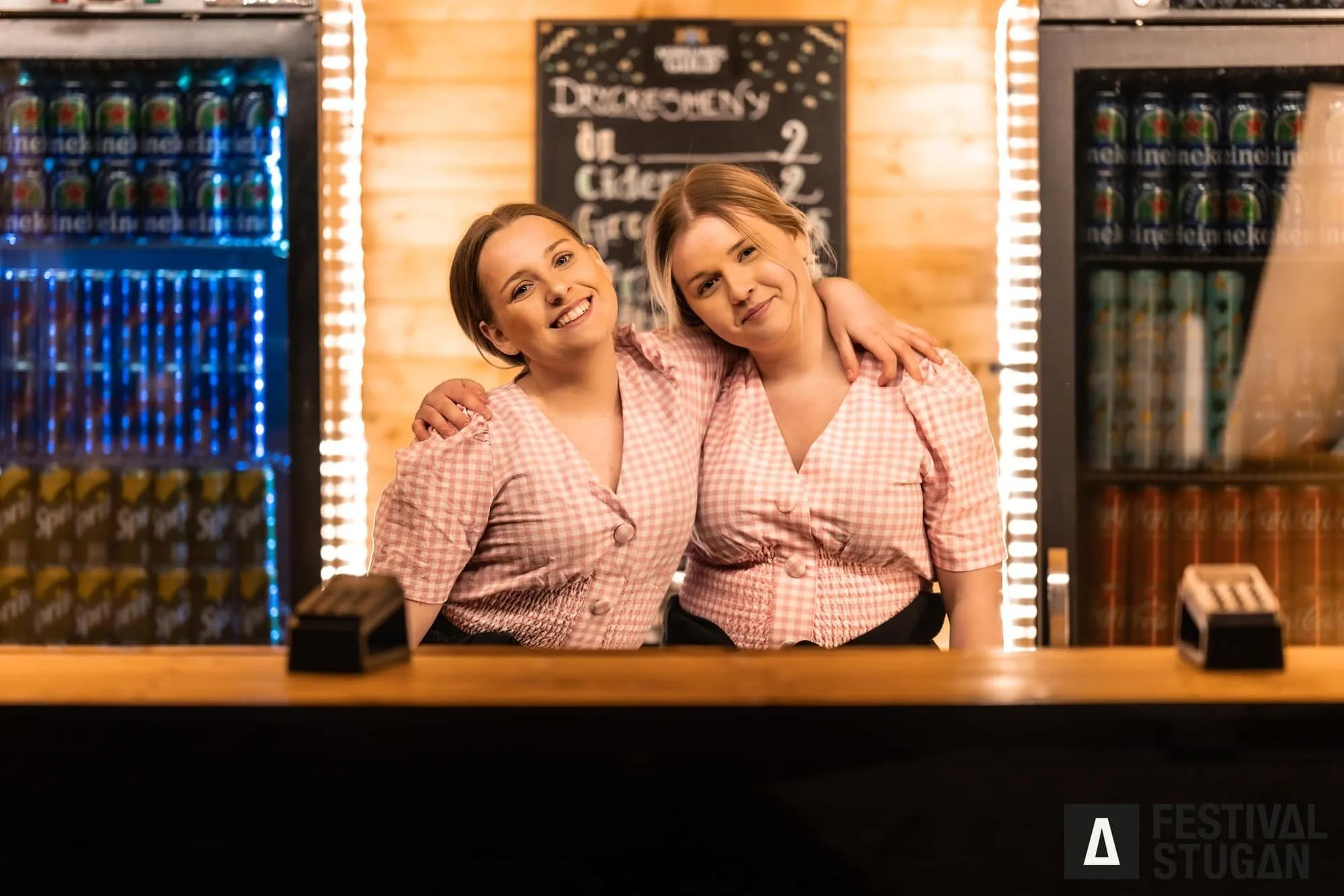 Två bartendrar bakom disken med dryckeskylar bakom sig