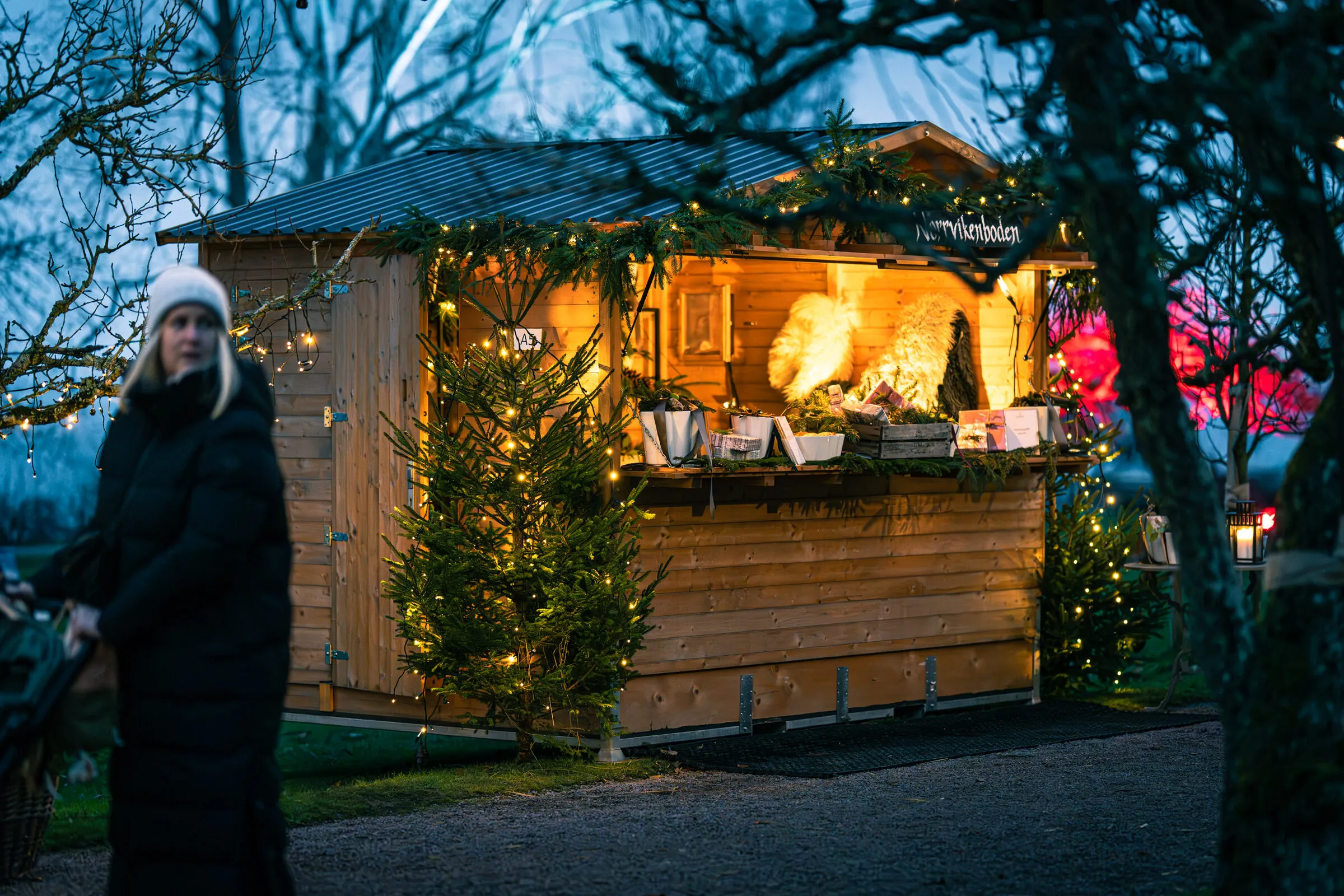 Julmarknadsstuga med granris, ljusslingor och en julgran framför