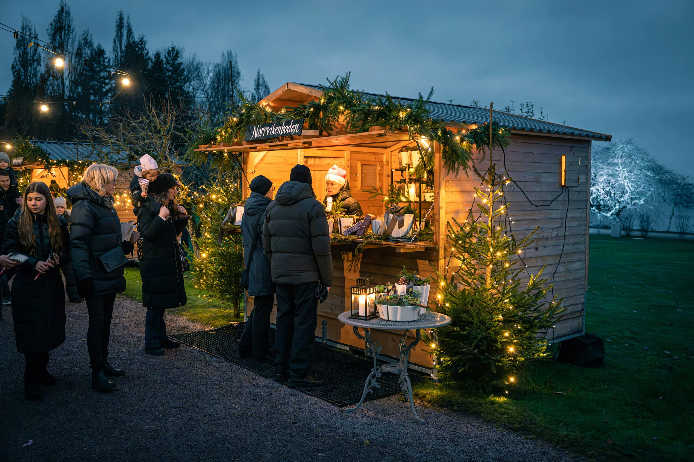 Besökare framför en upplyst julmarknadsstuga