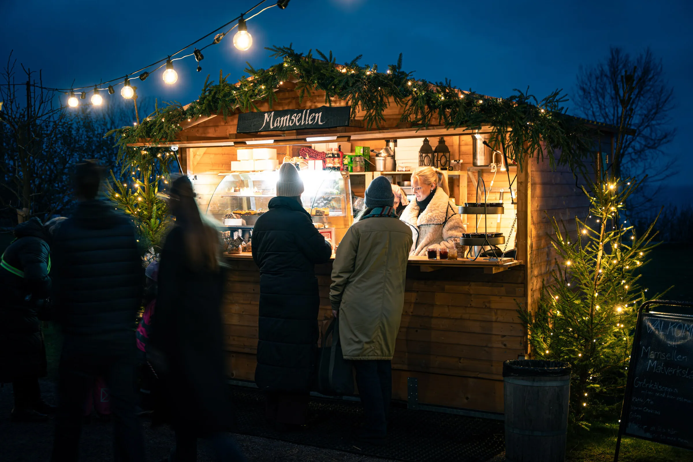 Besökare handlar vid en upplyst julmarknadsstuga
