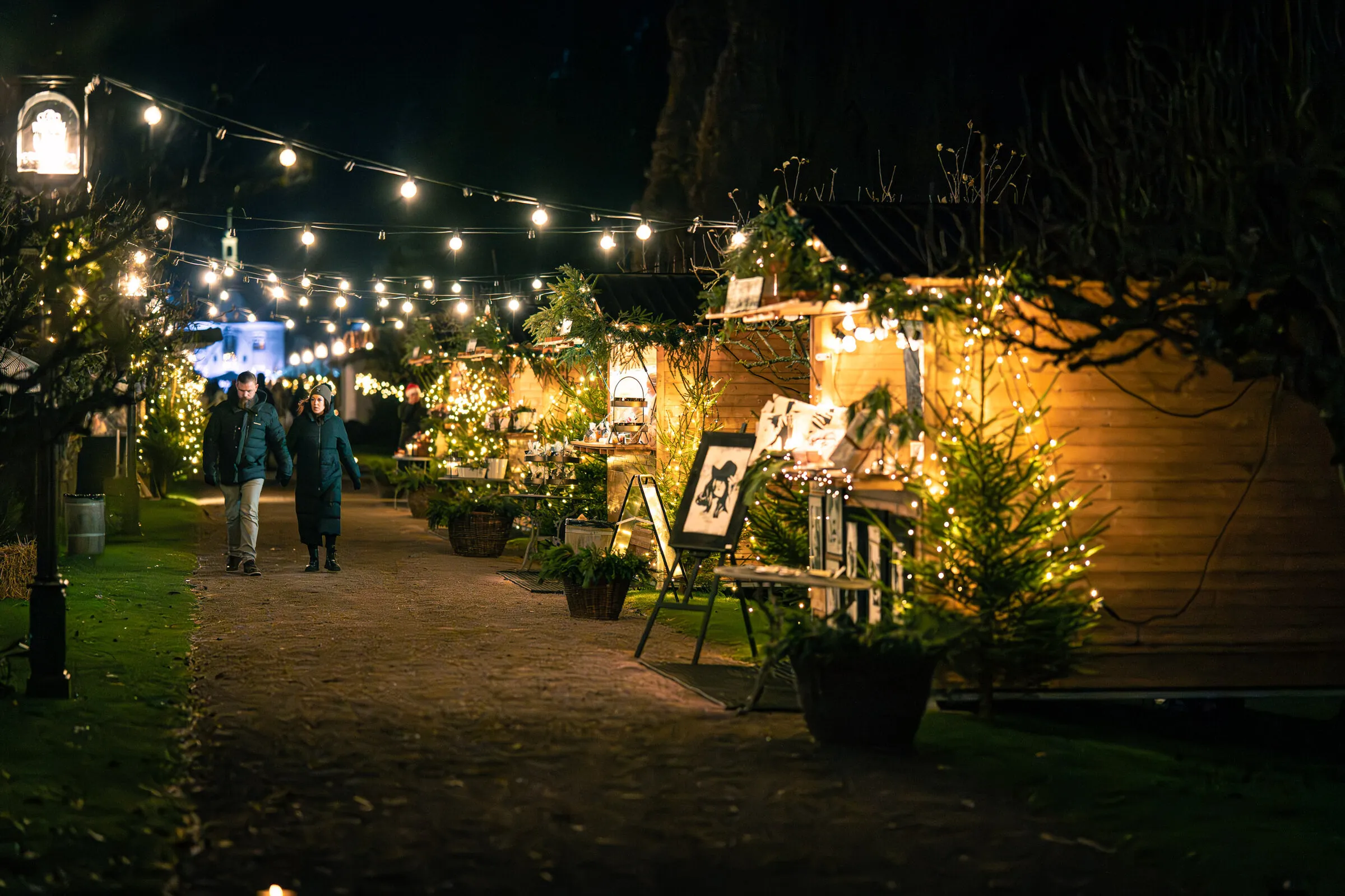 Julmarknadsstugor längs en grusgång med ljusslingor
