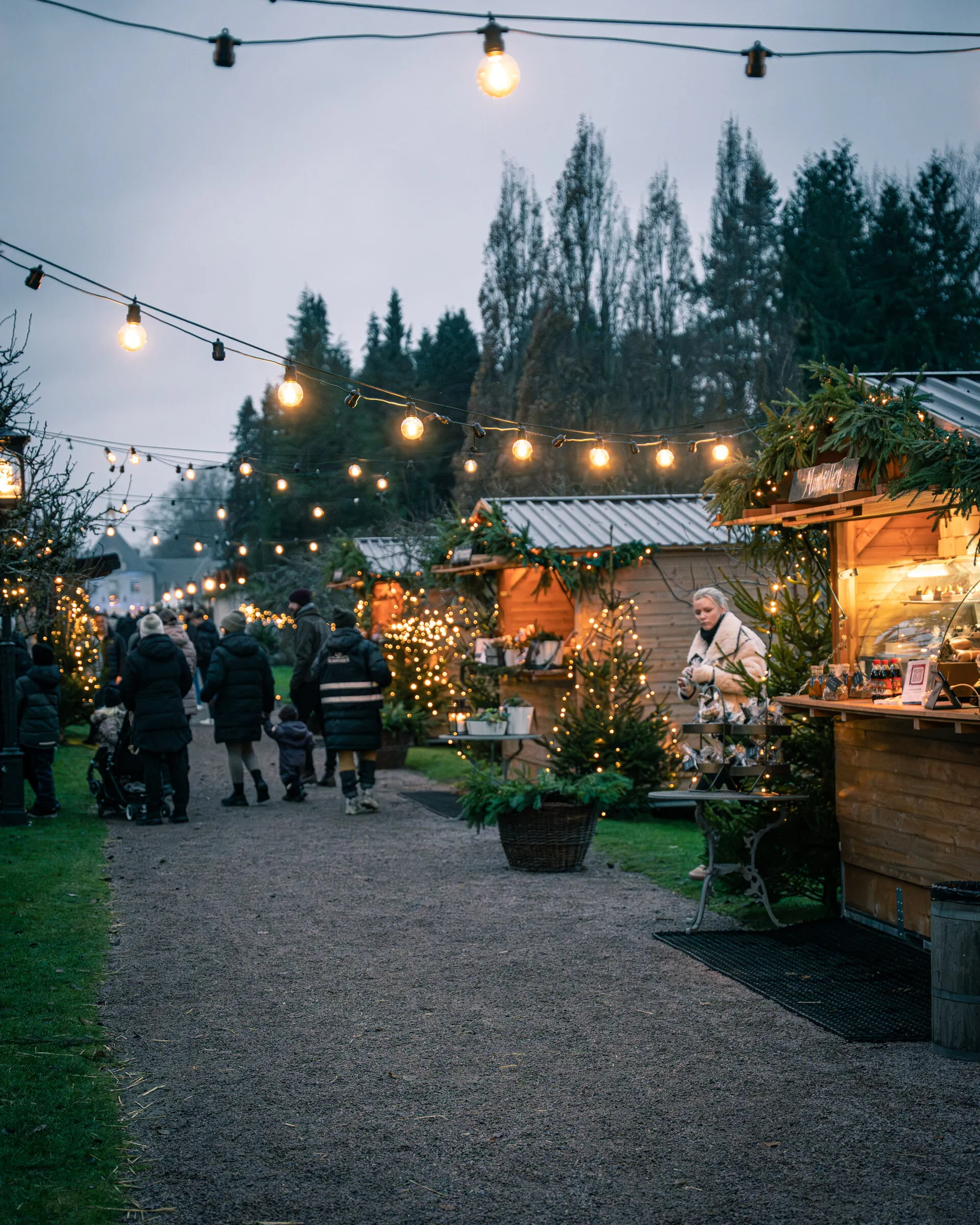 Rad av julmarknadsstugor längs en gång i skymningen